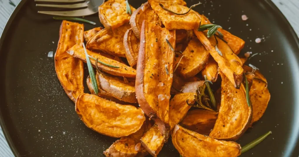 A close-up of golden, crispy roasted sweet potatoes with rosemary, showcasing their perfectly seasoned texture and vibrant color