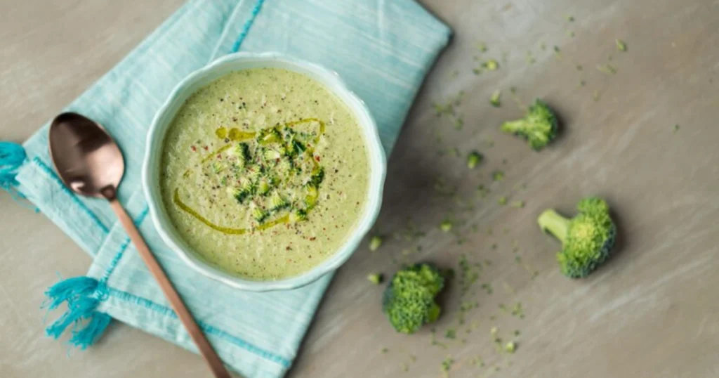 Warm bowl of Easy Healthy Chicken Broccoli Soup, featuring tender chicken pieces, vibrant green broccoli florets, and a light creamy broth, garnished with fresh parsley and served on a rustic wooden table with a slice of whole-grain bread.