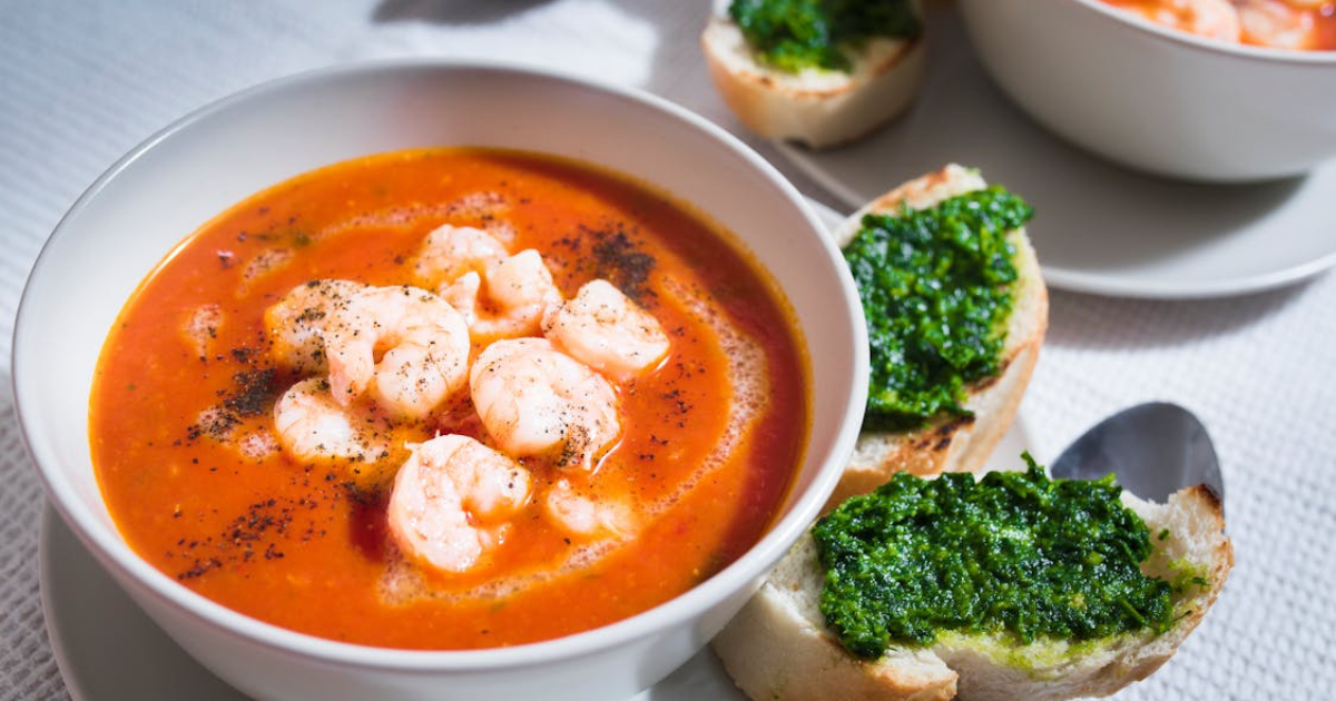 A steaming bowl of Tomato Shrimp Soup garnished with fresh basil, showcasing plump shrimp, vibrant tomatoes, and leafy greens in a rich, flavorful broth