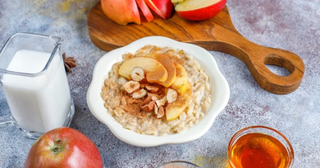 A warm bowl of Apple Cinnamon Oatmeal topped with nuts and a drizzle of maple syrup.